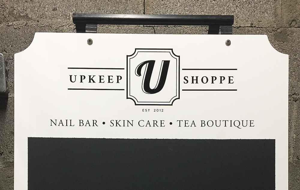 Cut vinyl signage for The Upkeep Shoppe on Preston St in Ottawa, ON. Logo, business hours, and sidewalk sandwich board graphics.